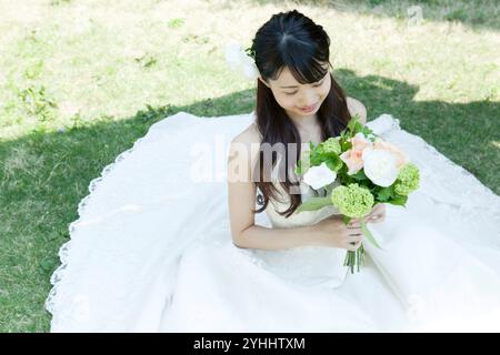 Jeune femme dans la robe de mariée tenant le bouquet et assis sur le patio Banque D'Images