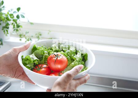 Main de femme tenant des légumes dans un bol dans la cuisine Banque D'Images