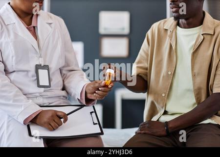 Gros plan du médecin féminin donnant bouteille avec pilules à un patient afro-américain pendant la consultation dans l'espace de copie clinique Banque D'Images