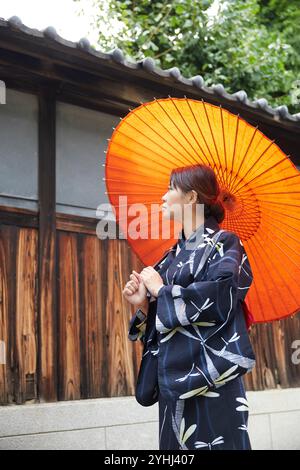 Femme en yukata marchant avec un parapluie japonais à côté d'une maison japonaise Banque D'Images