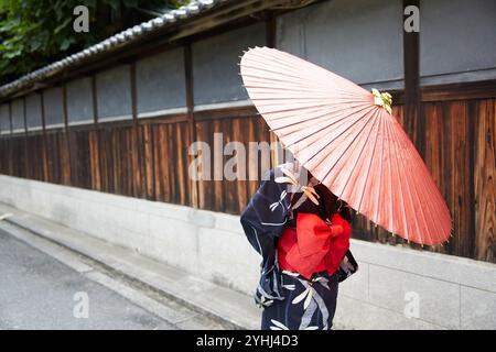 Femme en yukata marchant avec un parapluie japonais à côté d'une maison japonaise Banque D'Images