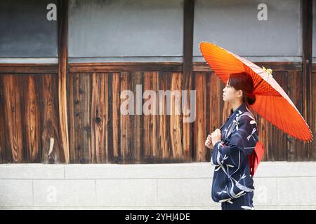 Femme en yukata marchant avec un parapluie japonais à côté d'une maison japonaise Banque D'Images