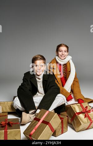 Deux enfants joyeux vêtus de tenues chaudes d'hiver profitent de la saison des fêtes avec des cadeaux de vacances. Banque D'Images