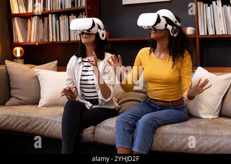 amis féminins multiraciaux profitant de l'expérience de réalité virtuelle sur le canapé confortable du salon, à la maison Banque D'Images