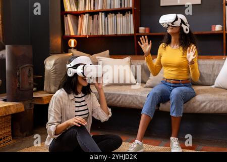 Amies féminines multiraciales profitant de l'expérience de réalité virtuelle à la maison, assis sur le sol Banque D'Images