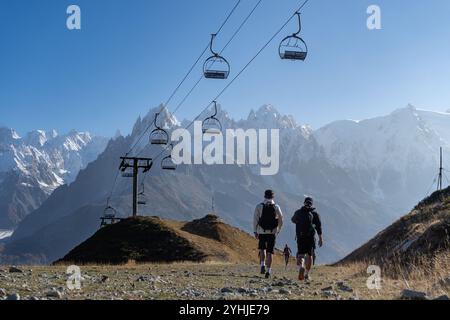 Deux randonneurs masculins marchant sous un télésiège STILL dans le parc naturel des aiguilles rouges, Chamonix, Alpes françaises. Chamonix aiguilles en arrière-plan. Banque D'Images