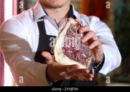 Le serveur tient un gros steak cru dans ses mains. Démonstration de steaks dans un restaurant. Le chef propose un steak dans un forfait. Le cuisinier prit un steak Banque D'Images