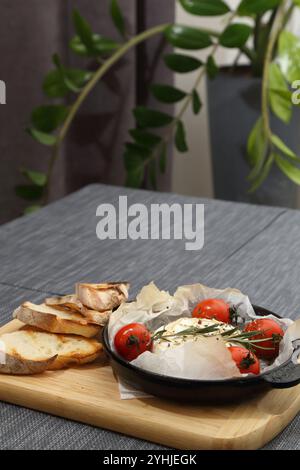 Camembert grillé avec tomates et pain grillé. Camembert dans une poêle à griller sur une planche de bois Banque D'Images