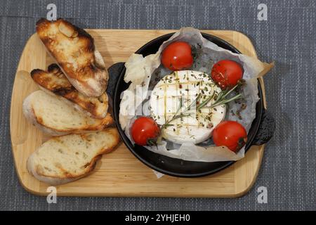 Camembert grillé avec tomates et pain grillé. Camembert dans une poêle à griller sur une planche de bois Banque D'Images