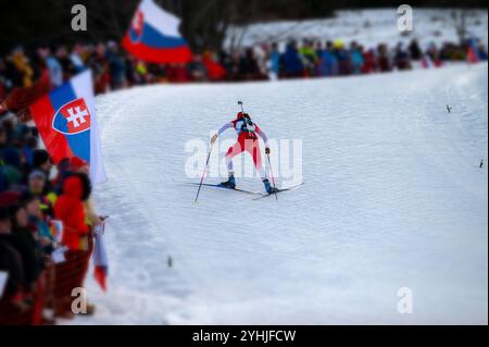 Une biathlète grimpe une pente raide et enneigée pendant une course professionnelle, tandis que la foule le long du parcours l'encourage et la soutient Banque D'Images