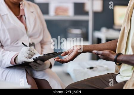 Vue latérale gros plan de l'homme afro-américain méconnaissable montrant une éruption cutanée sur le bras tout en consultant un dermatologue dans l'espace de copie clinique Banque D'Images