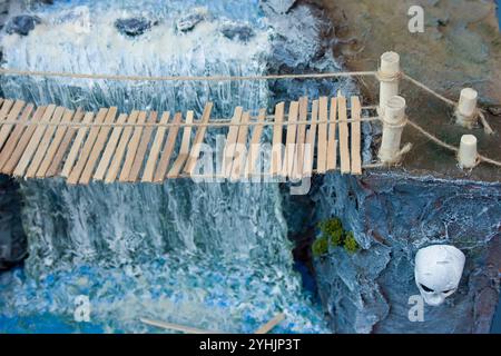 modèle diorama d'un pont de corde sur une rivière près d'une cascade et d'un crâne sculpté sur une falaise. Banque D'Images