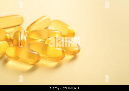 Gros plan d'une poignée de graisse de poisson d'huile de couleur dorée oméga-3 dans une capsule de gel souple sur fond jaune, espace de copie Banque D'Images