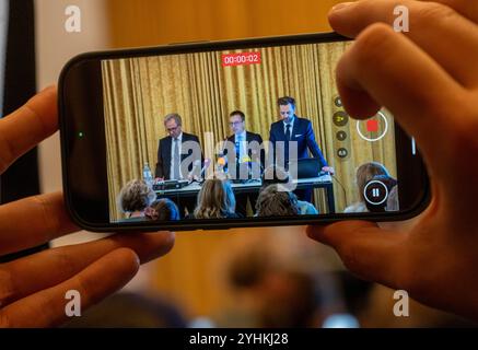 12 novembre 2024, Bavière, Munich : une personne filme les avocats du chef adjoint suspendu de la prison de Gablingen, Thomas Krimmel (gauche-droite), Alexander Stevens et Holm Putzke, sur un smartphone alors qu'ils donnent une conférence de presse. Après que des allégations de mauvais traitements contre le personnel pénitentiaire bavarois ont été révélées, les avocats de la défense de l'un des accusés portent des accusations contre le ministère de la Justice à Munich. Ils veulent divulguer des informations sur les abus dans le système carcéral. Photo : Peter Kneffel/dpa Banque D'Images