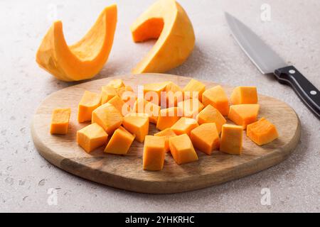 Citrouille coupée en morceaux sur une planche de bois sur un fond texturé beige Banque D'Images
