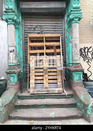 Une scène urbaine avec de vieilles palettes en bois appuyées contre une entrée de bâtiment usée. Colonnes turquoise altérées et peinture écaillée. Banque D'Images