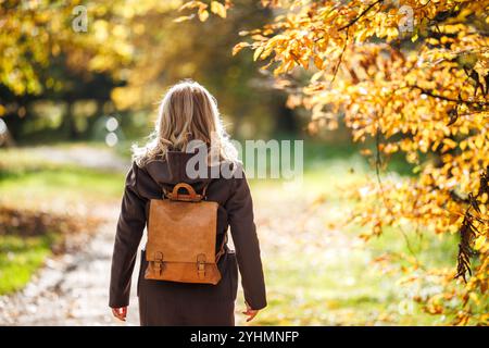 Femme élégante avec manteau brun et sac à dos promenades dans le parc d'automne. Beauté et mode de vie Banque D'Images