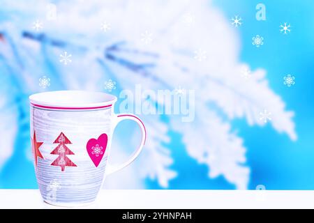 Carte de voeux de Noël. Grande tasse d'hiver blanche avec café, décorée avec des arbres de Noël rouges, des coeurs et des étoiles sur des branches enneigées et de la neige Banque D'Images