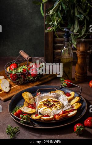 Délicieux camembert cuit au four avec des fraises, du miel, du romarin et du pain grillé sur un plateau vintage Banque D'Images