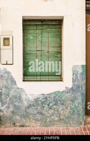 Ancienne façade ébréchée avec fenêtre et store vert en Espagne. Banque D'Images