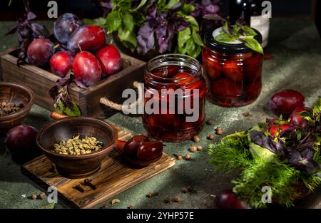 Les prunes marinées maison sont préparées dans des bocaux en verre avec du basilic frais, de l'aneth, de la cardamome, des clous de girofle et des grains de poivre Banque D'Images