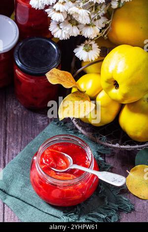 Confiture de coings dans un bocal en verre, coings dans un panier et bouquet de chrysanthèmes. Nature morte d'automne, style rustique, mise au point sélective. Banque D'Images