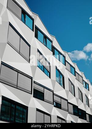 Immeuble de bureaux moderne contre le ciel bleu. Façade argentée de forme géométrique polygonale avec volets roulants de fenêtre. Banque D'Images