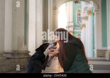 Une jeune femme interagit avec son chien dans une arche historique, avec la lumière qui y pénètre. L'image capture le lien entre eux dans un cadre serein et élégant Banque D'Images