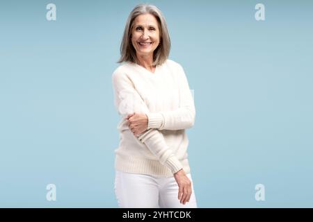 Portrait de belle, positive senior, femme aux cheveux gris portant des vêtements décontractés, mannequin posant, debout isolé sur fond bleu. Shopping Banque D'Images