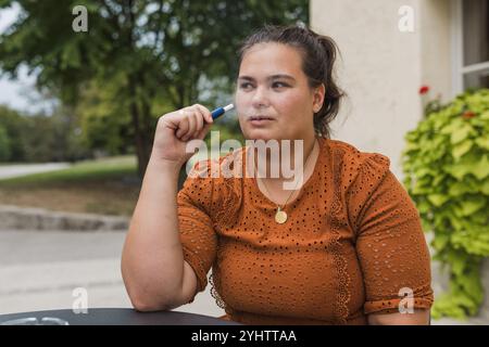 Femme souriante pendant une pause cigarette, profitant de vapoter à l'extérieur. Concepts de produits du tabac chauffés et modes de vie modernes. Banque D'Images