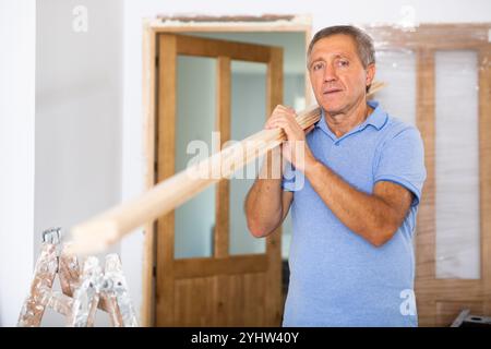 Menuisier mâle d'âge moyen en uniforme tenant des planches de bois à l'intérieur Banque D'Images