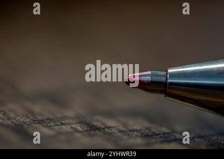 Un stylo avec une pointe rouge se trouve sur une surface sombre. Le stylo est le seul objet de l'image Banque D'Images