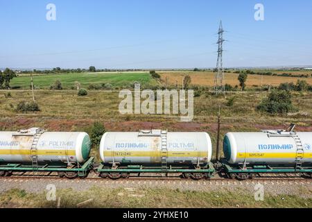 Les wagons-citernes blancs et jaunes étiquetés « POLYMIR » se déplacent le long d'une voie ferrée dans un paysage rural de Roumanie Banque D'Images