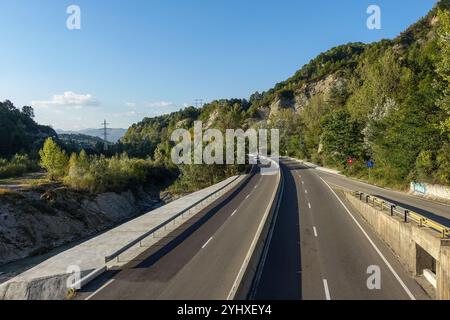 Autoroute de montagne vide 1 près de Sinaia, Roumanie, serpentant à travers des collines boisées sous un ciel bleu clair par une journée ensoleillée Banque D'Images