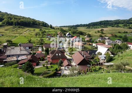 Vue panoramique sur le village pittoresque de Banský Studenec niché dans des collines verdoyantes sous un ciel bleu clair, avec de charmantes maisons et une végétation luxuriante Banque D'Images