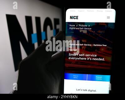 Allemagne. 10 juillet 2024. Dans cette illustration photo, une personne tient un téléphone portable avec la page Web de la société israélienne de logiciels CRM NICE Ltd devant le logo de l'entreprise. Crédit : SOPA images Limited/Alamy Live News Banque D'Images