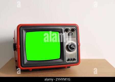 Téléviseur rétro avec écran vert sur table en bois près du mur blanc, espace pour le design. Touche Chroma Banque D'Images