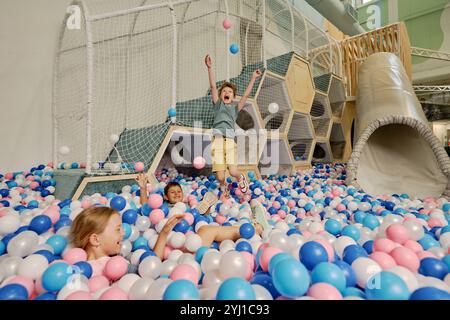 Enfants excités jetant et attrapant des ballons de couleurs blanc, bleu et rose tout en s'amusant sur une aire de jeux moderne Banque D'Images