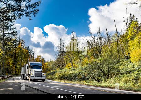 Semi-camion industriel à capot classique Big Rig blanc avec cabine allongée pour le repos du conducteur de camion transportant des marchandises dans une semi-remorque en vrac conduisant sur la route Banque D'Images