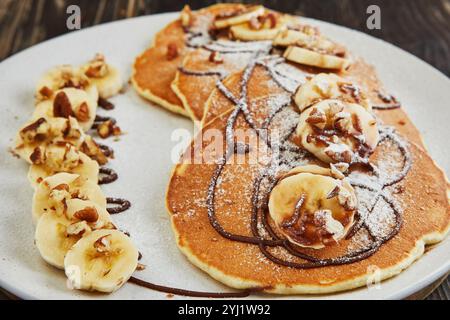 Délicieuses crêpes garnies de bananes tranchées, de noix hachées et de filet de chocolat, créant un plat délicieux et visuellement attrayant pour le petit déjeuner. Banque D'Images