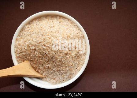 Écailles de psyllium servies dans un bol blanc avec une cuillère en bois, parfaites pour les thèmes de santé et de bien-être. Banque D'Images