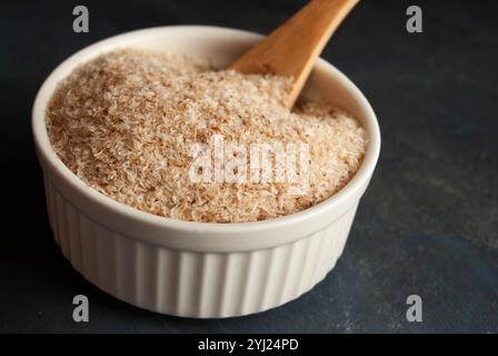 Enveloppe de psyllium naturelle avec une cuillère en bois dans un bol blanc, idéale pour les visuels diététiques ou biologiques. Banque D'Images