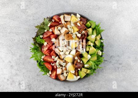 Salade classique de Cobb américain avec tomates, bacon, poulet, œufs, avocat et fromage bleu sur fond gris. Vue de dessus. Copier l'espace. Banque D'Images