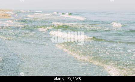 Image rapprochée d'une mer calme avec des vagues se lançant doucement sur une plage de sable. Belle vague bleue douce pause plage vide. Lever du soleil. Les vagues de mer s'écrasent sur le rivage Banque D'Images