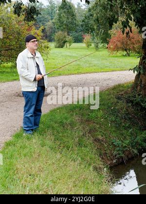 Homme mûr pêchant dans un étang tranquille entouré de verdure luxuriante, Italie Banque D'Images