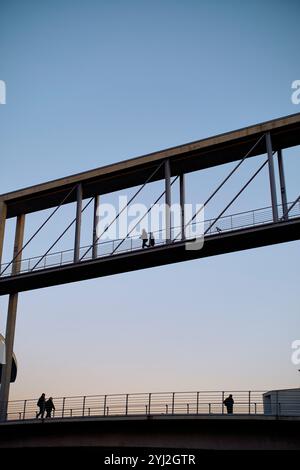 Silhouettes de personnes marchant sur un pont piétonnier moderne contre un ciel crépusculaire clair, Berlin, Allemagne Banque D'Images