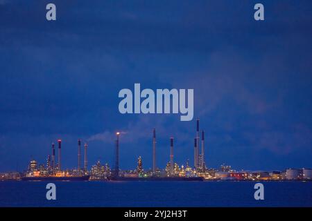 Horizon industriel au crépuscule avec des tours de raffinerie illuminées contre un ciel bleu profond, Singapour Banque D'Images