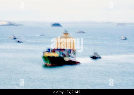 Navire cargo flou en mouvement chargé de conteneurs colorés sur une mer calme avec d'autres bateaux en arrière-plan, Singapour Banque D'Images