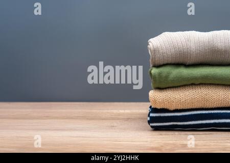Une pile de vêtements soigneusement pliés sur une table en bois sur un fond gris. Copier l'espace pour le texte. Banque D'Images