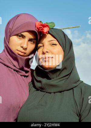 Deux femmes en hijabs posant contre un ciel clair, dont une avec une fleur rouge ornée sur son foulard, Maroc Banque D'Images